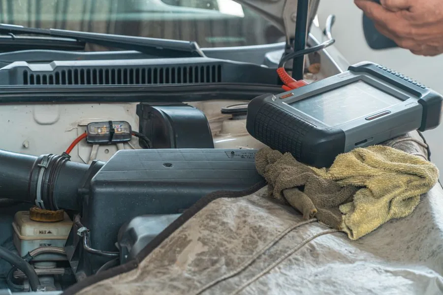 A diagnostic tablet plugged into a car with the hood up